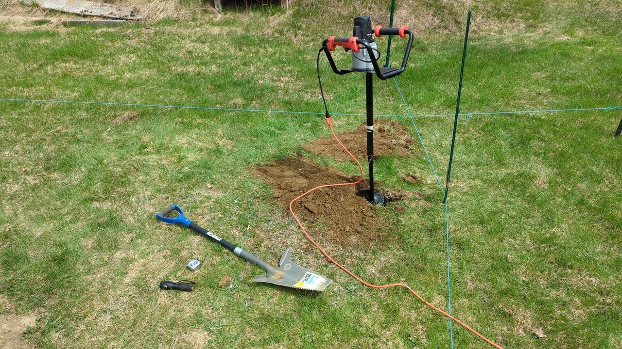 Post hole digger stuck in a hole next to a shovel and some other tools