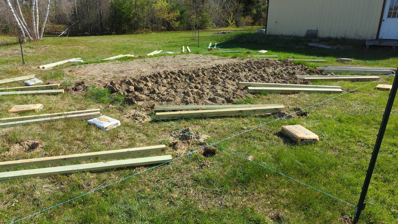 Fence posts, braces, and concrete mix laying next to holes ready for installation