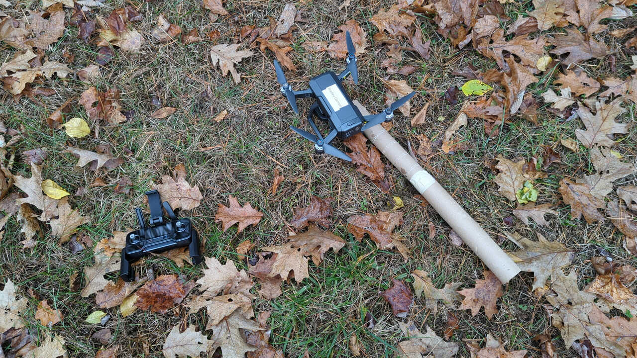 My quadcopter on the ground next to its controller and with the paper towel roll extender arm attached to one of its legs