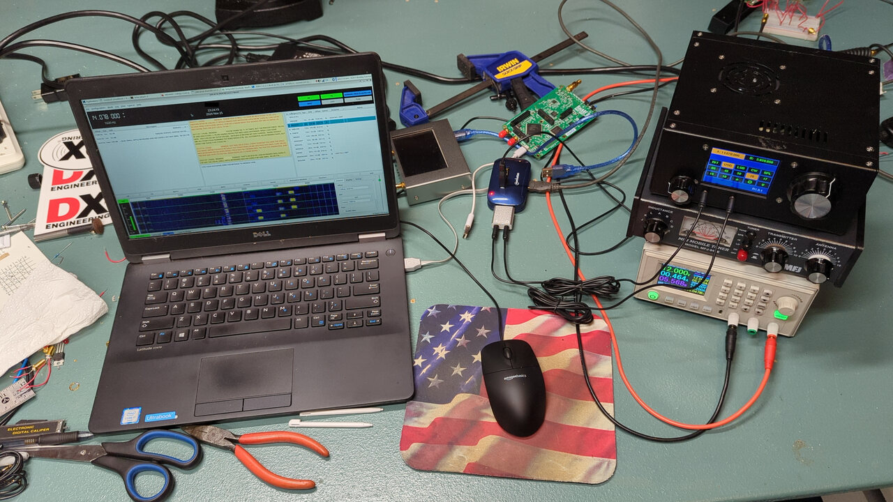 Laptop running JS8Call with a DC power supply, manual tuner, and uBITX transceiver running on 20 m, all sitting on a cluttered lab bench