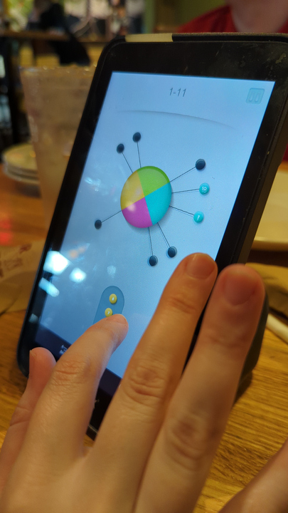 A hand
ready to tap a small touchscreen showing a colored circle with several pins sticking out of it, all
on top of a restaurant table