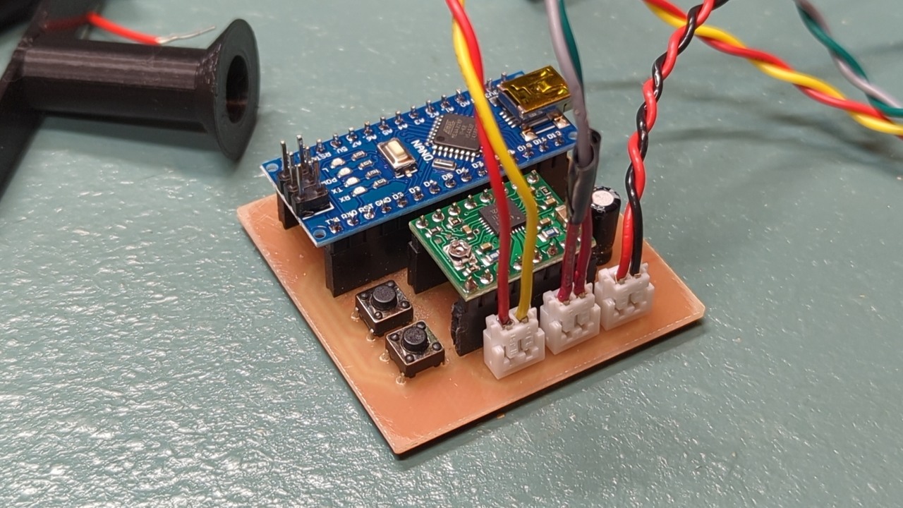 A small square circuit board with an Arduino Nano, a stepper driver, some buttons, and some off-board connectors sits on a workbench