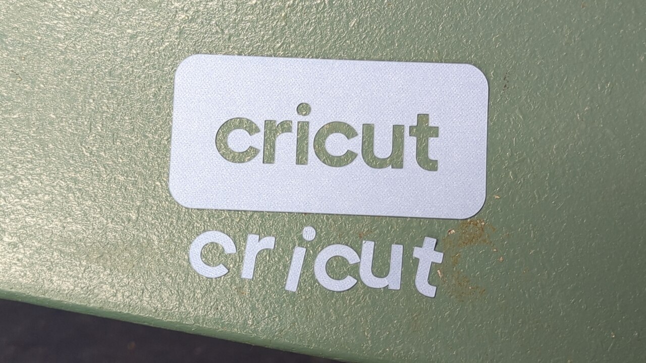 A rounded rectangle of blue cardstock with the word “cricut” cut into it, along with the cut out letters scattered nearby