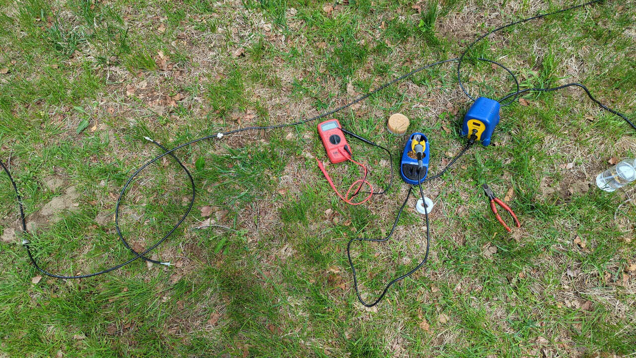 A soldering iron, some coax cables, a multimeter, and various other tools laying in the grass