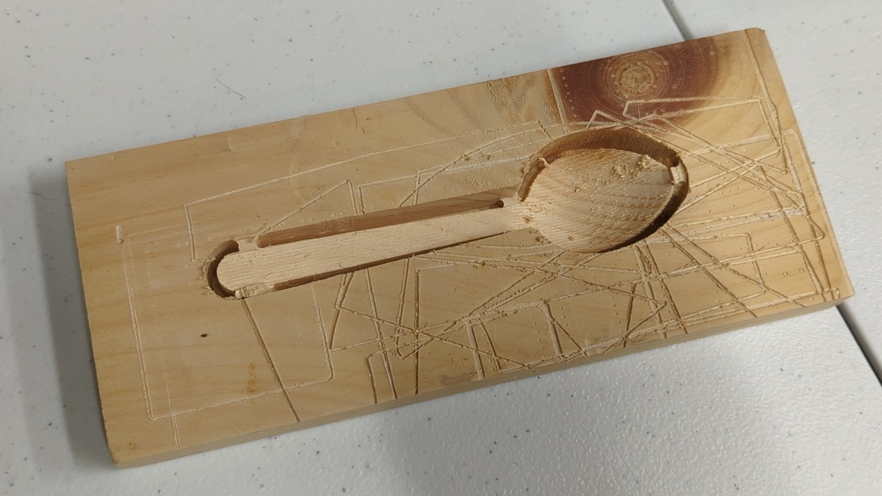 Spoon-shaped cutout in a piece of 1×4 pine with distinct contour lines along the spoon’s long axis