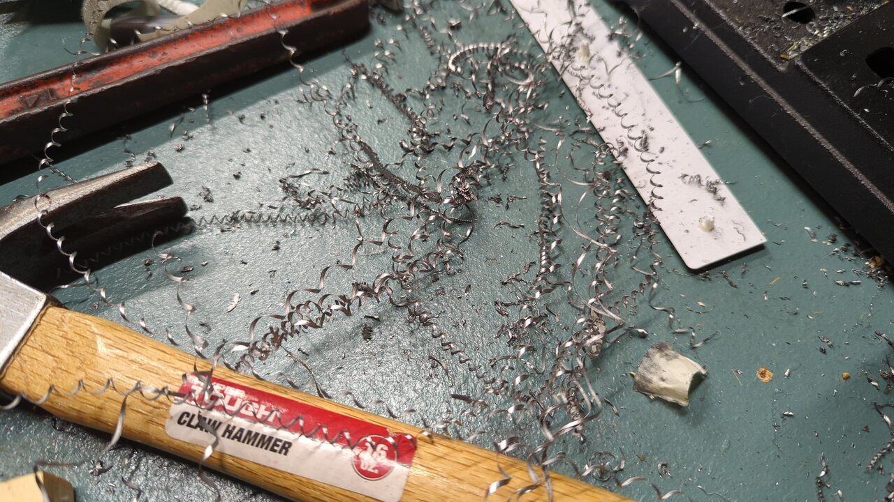 A big mess of spiral steel chips and smaller bits of detritus on a table. Various hand tools have been partially buried by the chips.
