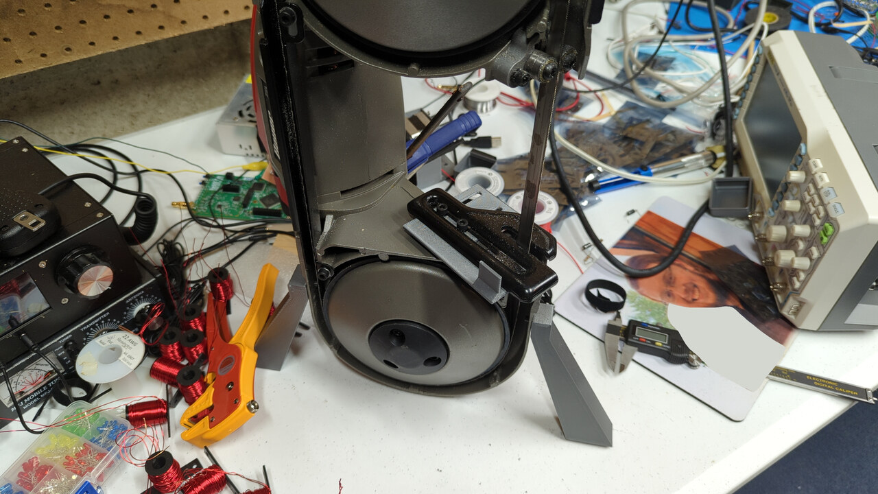 A portable band saw with 3D printed supports stands somewhat unsteadily in an upright position on a table.