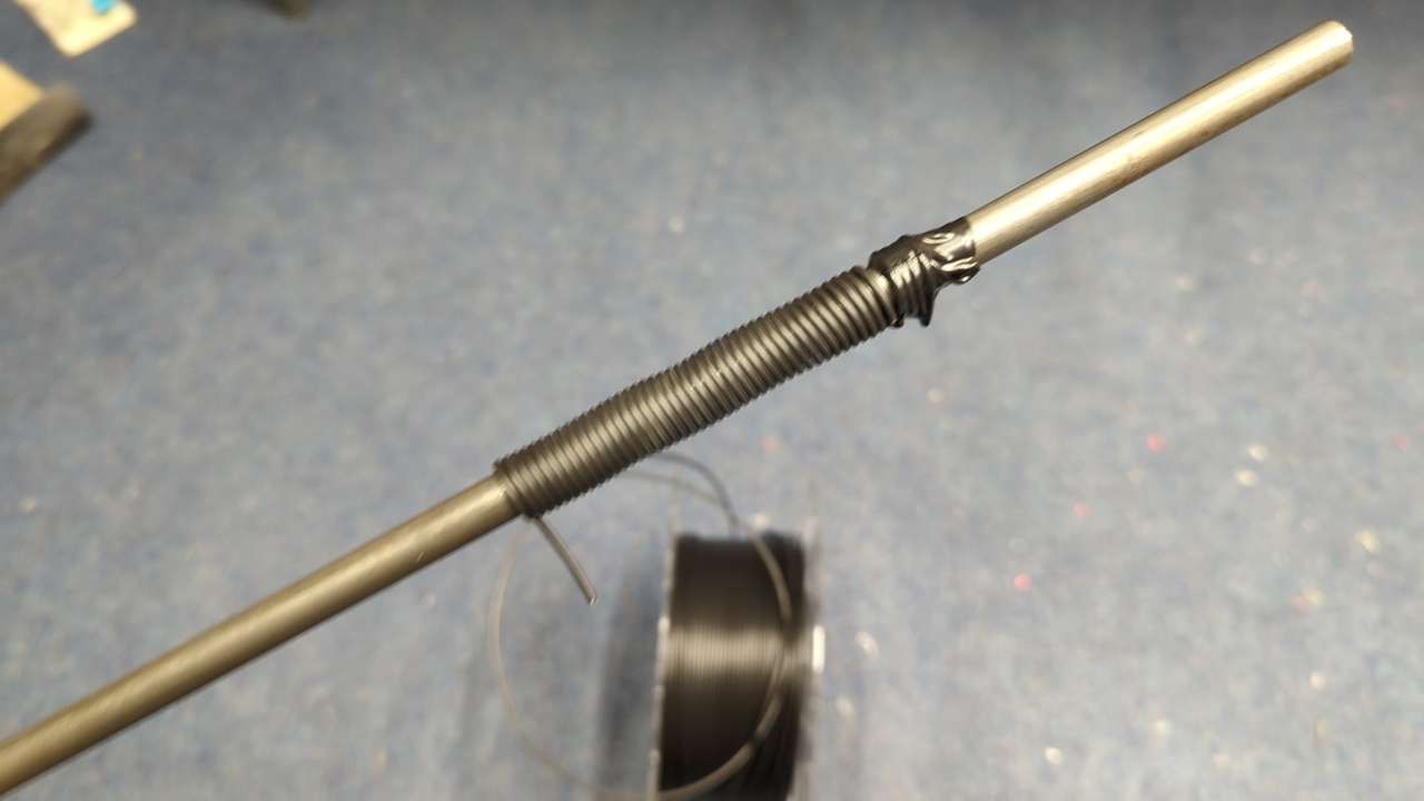 Several turns of black 3D printer filament wound around a 3/8” steel rod. I’ve secured the filament to the rod on one end with electrical tape.