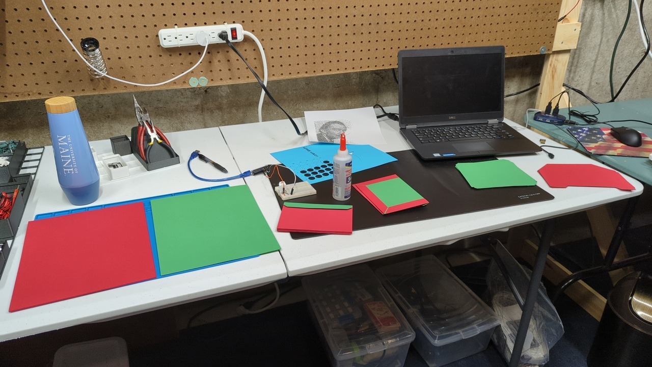 Lab bench with various red and green paper, glue, a stack of envelopes, and my laptop