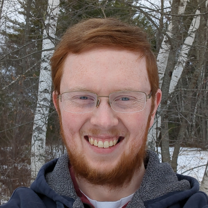 Headshot of me, smiling in front of some birch trees on a snowy January day