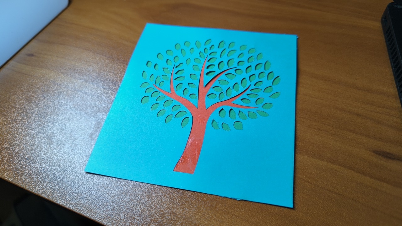A stack of laser-cut pieces of construction paper. The papers are each a different color, and the laser-cut regions reveal a pattern in the form of a beautiful tree.
