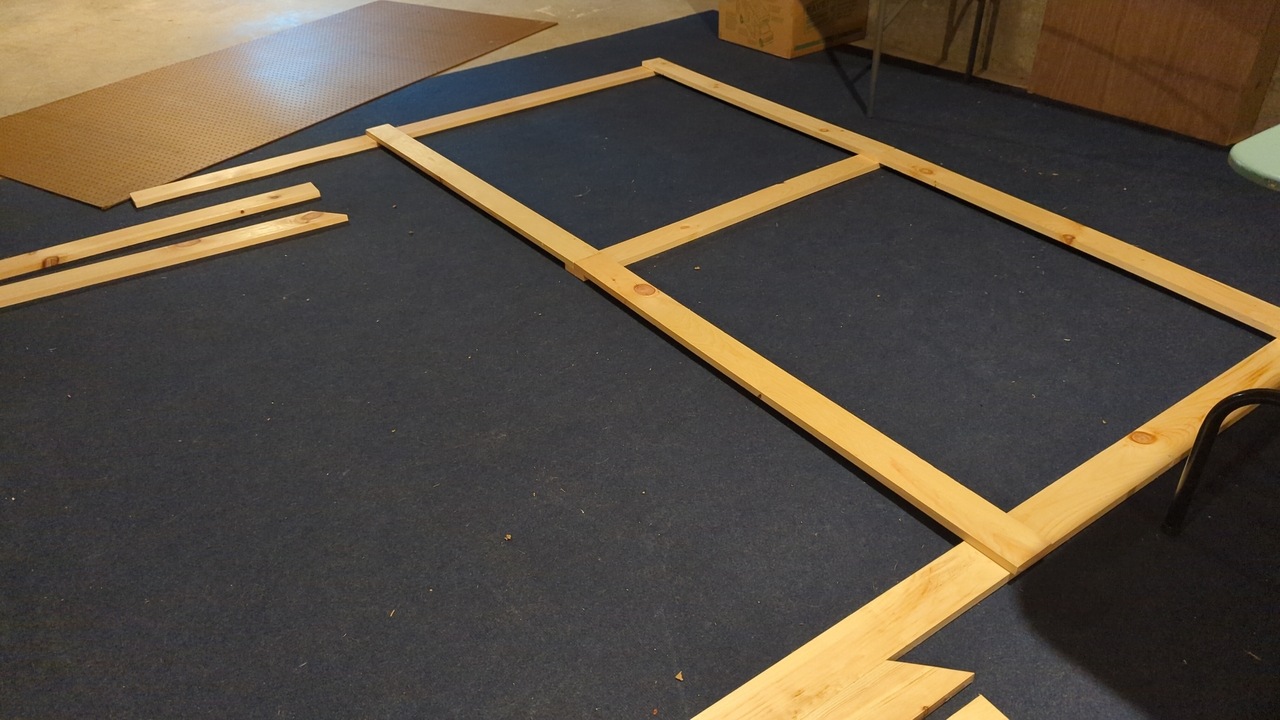 Pegboard frame laid out on the floor during assembly with the pegboard sheet itself laying nearby
