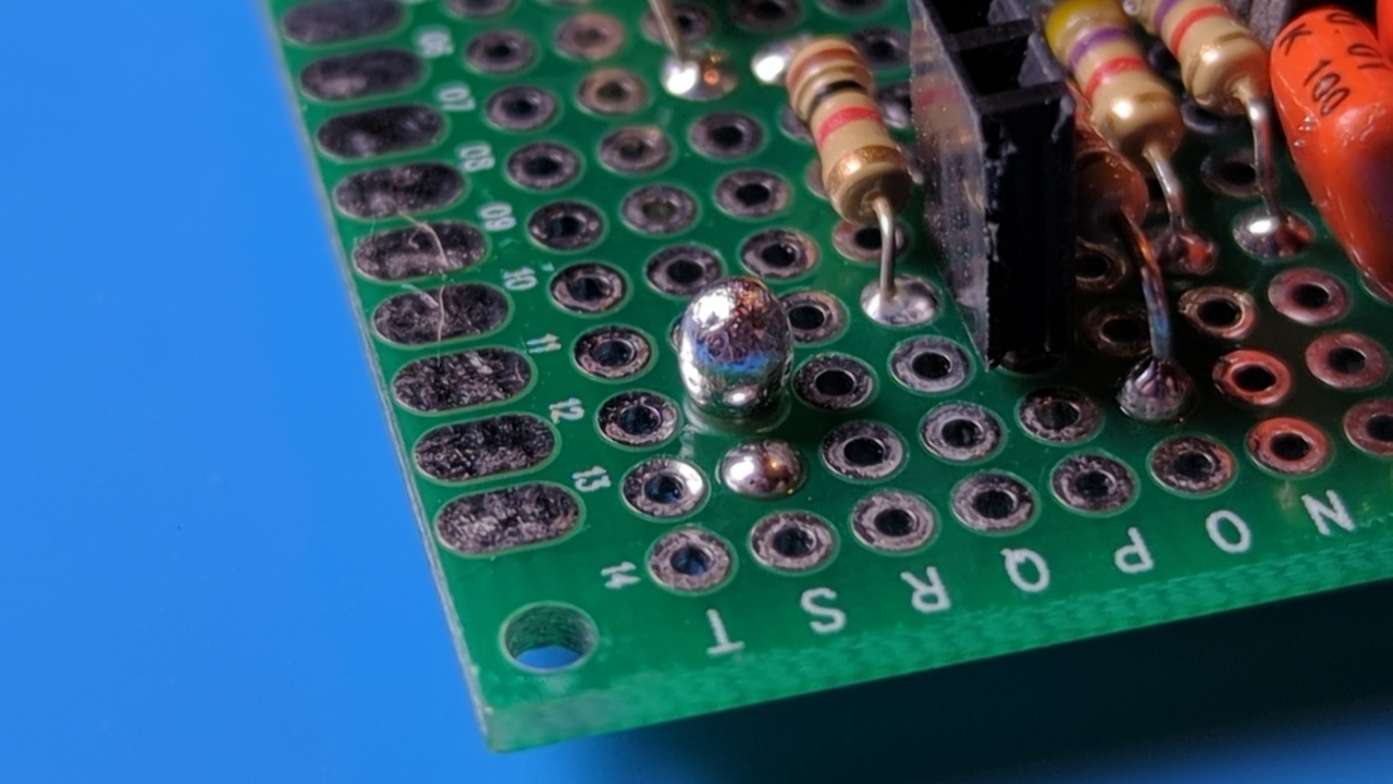 Close-up of the failed protoboard with a large blob of solder sticking up from one of the holes