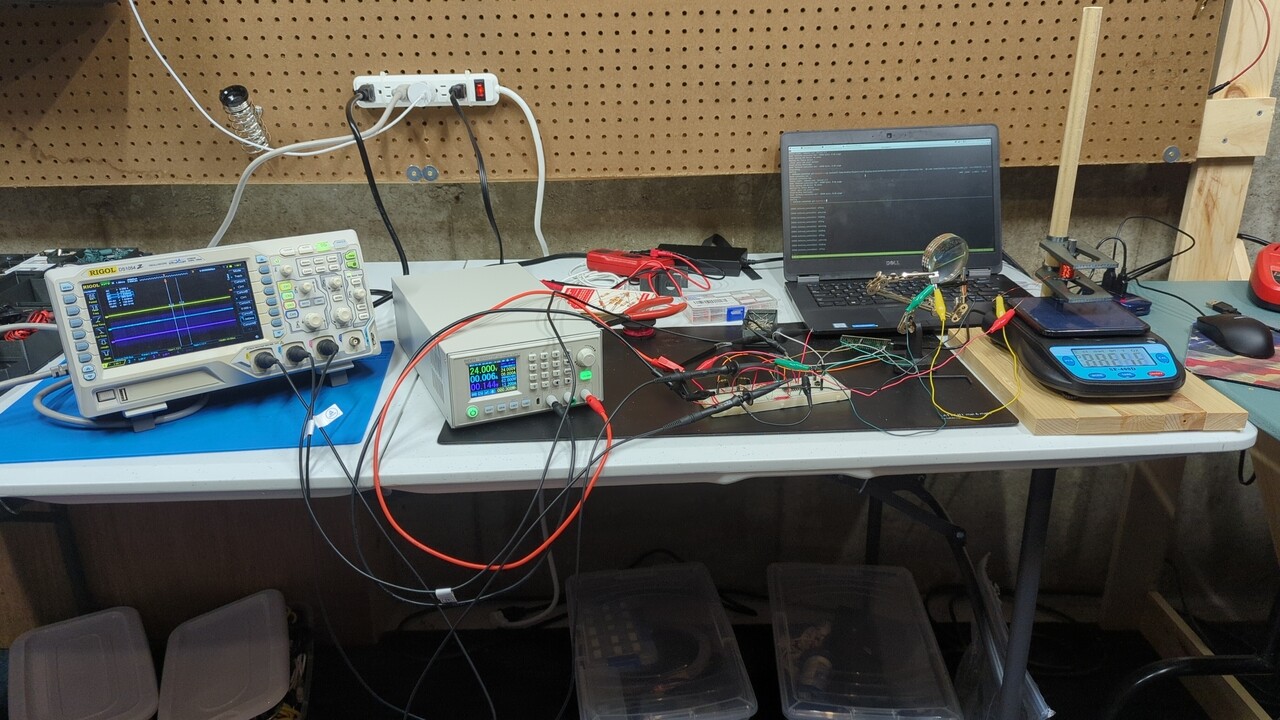 A part of my lab bench with an oscilloscope, DC power supply, a breadboard with lots of wires, a laptop, a solenoid test stand for measuring force, and a solenoid under test